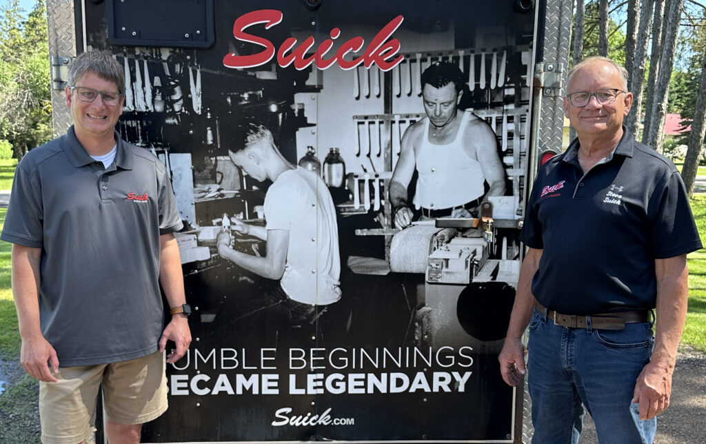 Ever mindful of their family company’s history, the new owner of Suick Lure Company, Mike Suick (left) and his father, Steve, stand in front of a trailer adorned with a photo of John and Frank Suick making lures in their shop in the 1940s. The trailer is used by Suick Lure Company when it exhibits at sports shows.