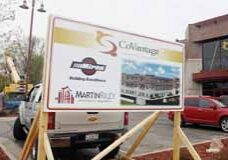 Heavy equipment can be seen behind the sign announcing the construction project, along with an artist’s rendering of the completed project, at CoVantage Credit Union.